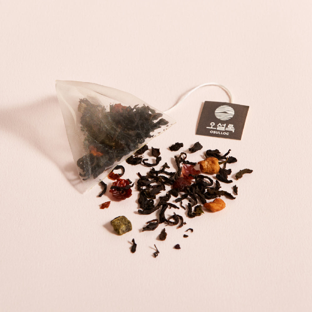 OSULLOC Cherry Blossom Tea — Pyramid tea bag and scattered loose blend on a pink surface.