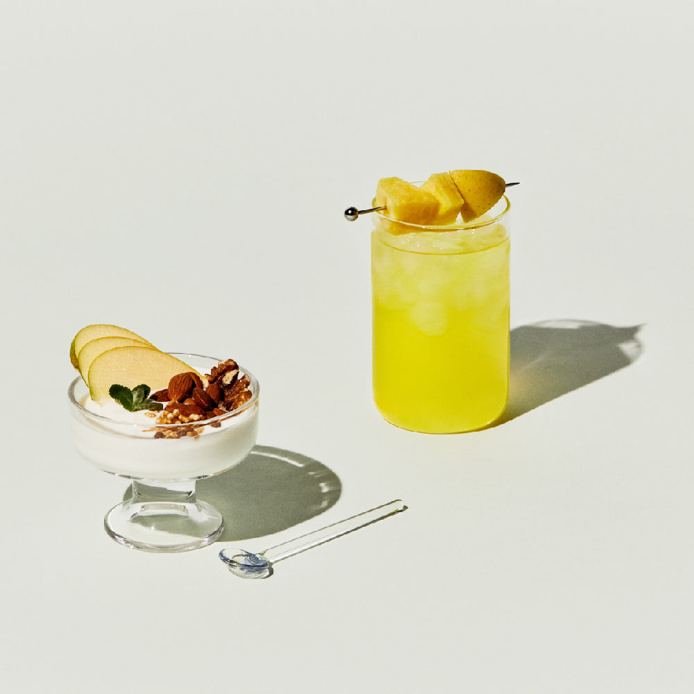 OSULLOC Kombucha Apple Pine — Yellow iced drink beside a small bowl with fruit and a crunchy topping.