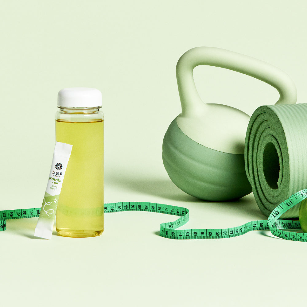 OSULLOC Kombucha Apple Pine — Bottled drink and individual stick beside a kettlebell, rolled exercise mat and measuring tape.