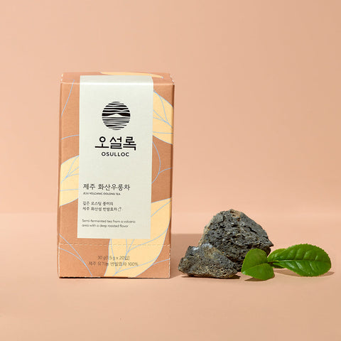 OSULLOC Jeju Volcanic Oolong Tea — Terracotta-coloured box beside dark rocks and green leaves.