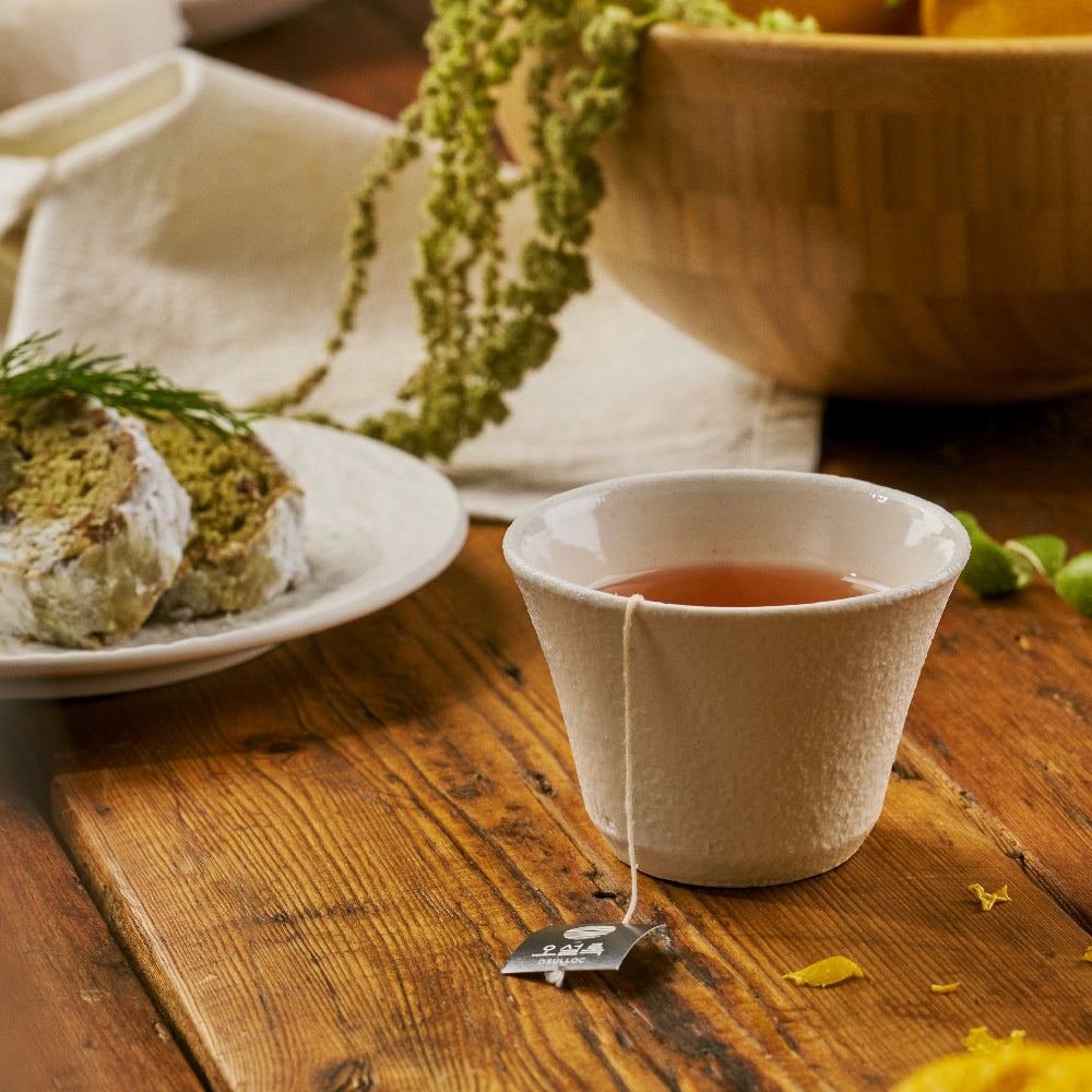OSULLOC Signature Earl Grey — Tea in a ceramic cup beside slices of cake on a wooden table.