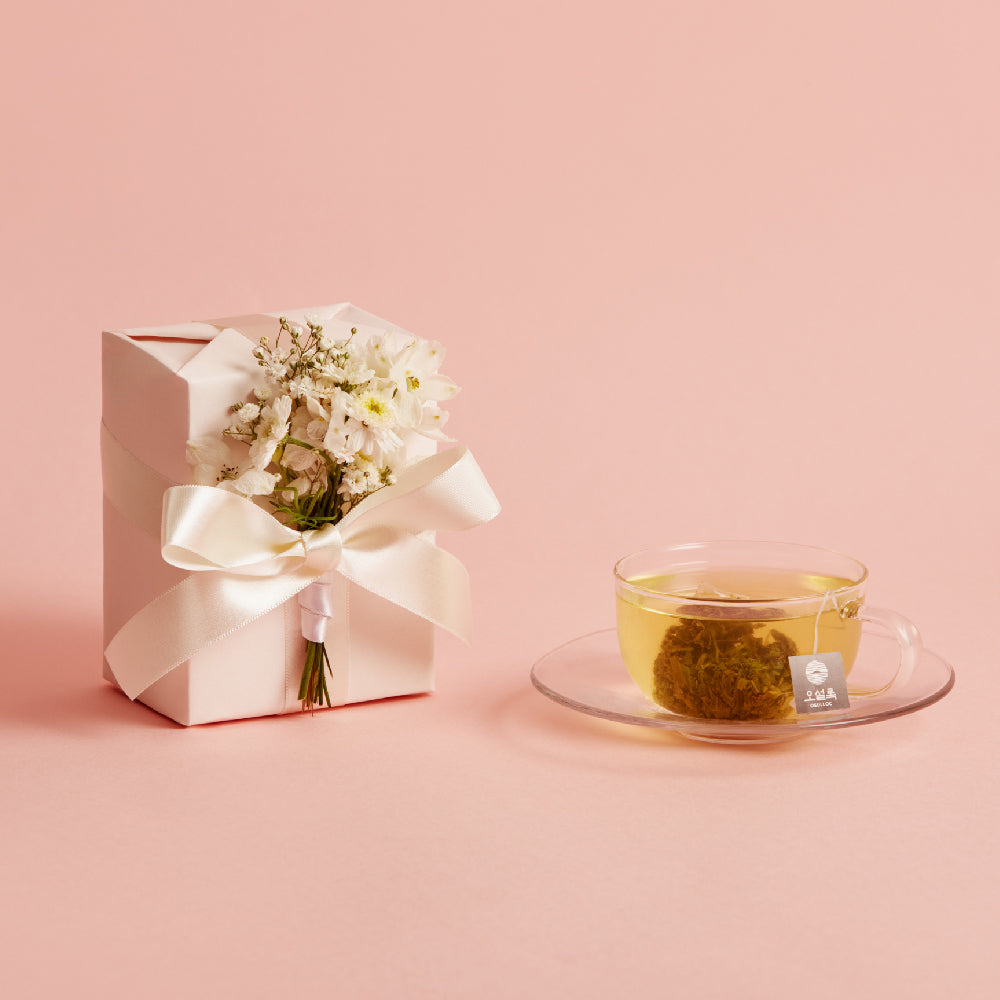 OSULLOC Wedding Green Tea — Ribbon-tied white box with small flowers beside a glass cup of tea on pink.