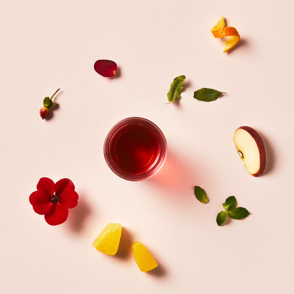 OSULLOC Hibiscus Sunshine — Overhead view of red infusion surrounded by fruit, leaves and petals.