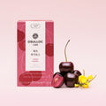 OSULLOC Cherry Rooibos Tea — Red rooibos box beside cherries and yellow flowers on pink.