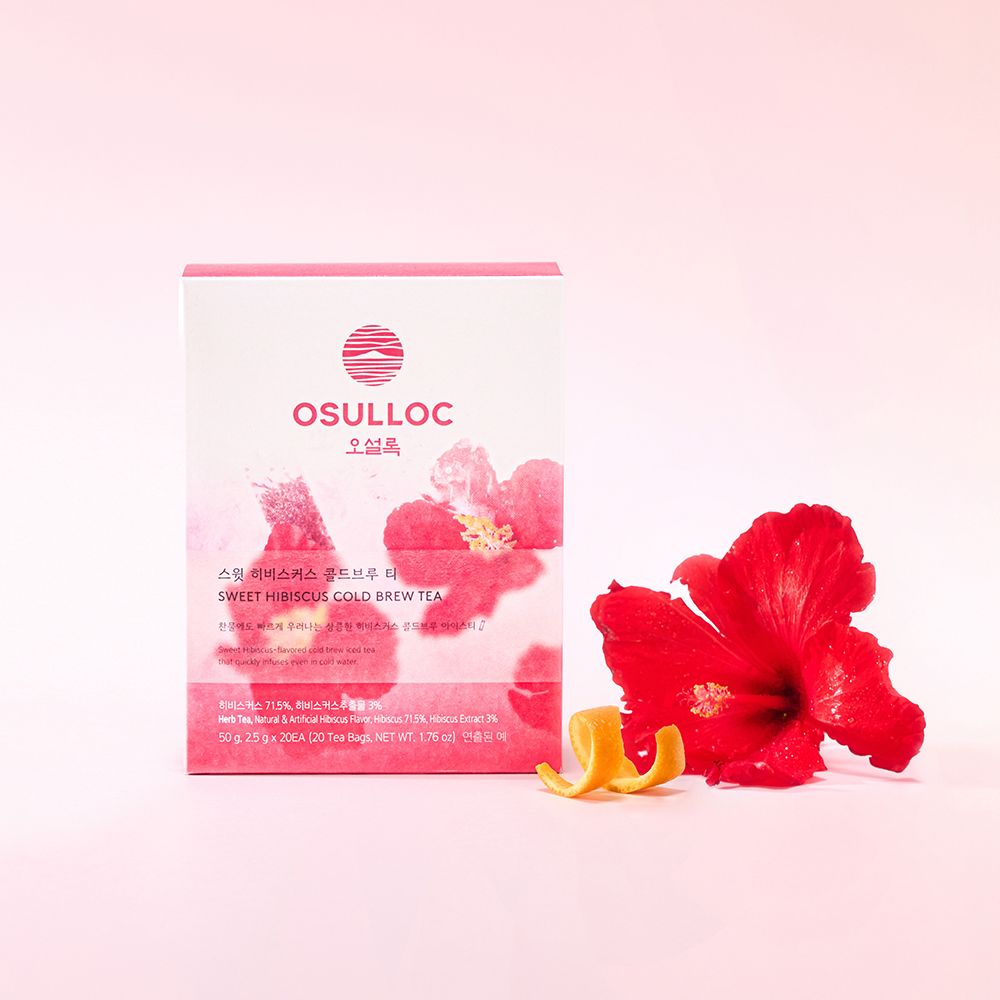 OSULLOC Sweet Hibiscus Cold Brew Tea — Caja rosa y blanca de infusión en frío junto a una flor roja de hibisco y piel de cítrico.