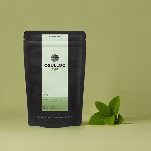 OSULLOC Sejak Green Tea — Dark Sejak pouch beside fresh green leaves on an olive background.