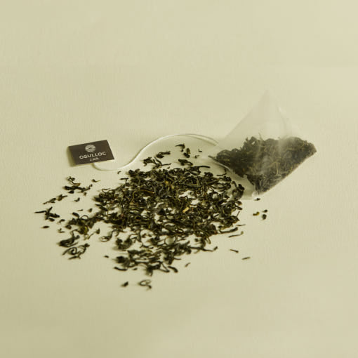 OSULLOC Sejak Green Tea — Pyramid tea bag beside scattered green tea leaves.