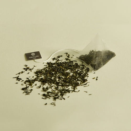 OSULLOC Sejak Green Tea — Pyramid tea bag beside scattered green tea leaves.