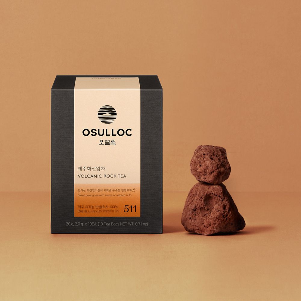 OSULLOC Jeju Volcanic Rock Tea — Caja oscura con etiqueta naranja junto a rocas porosas apiladas.