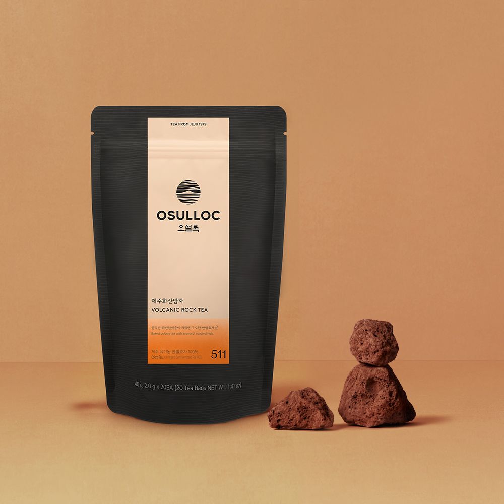 OSULLOC Jeju Volcanic Rock Tea — Bolsa oscura con etiqueta naranja junto a pequeñas rocas porosas.