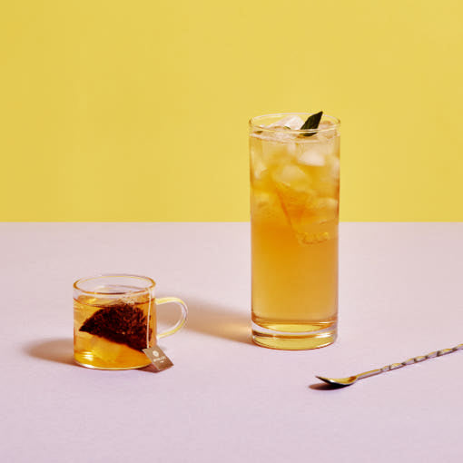 OSULLOC Peach Papaya Black Tea — Tall glass of iced tea beside a small cup with a steeping tea bag.