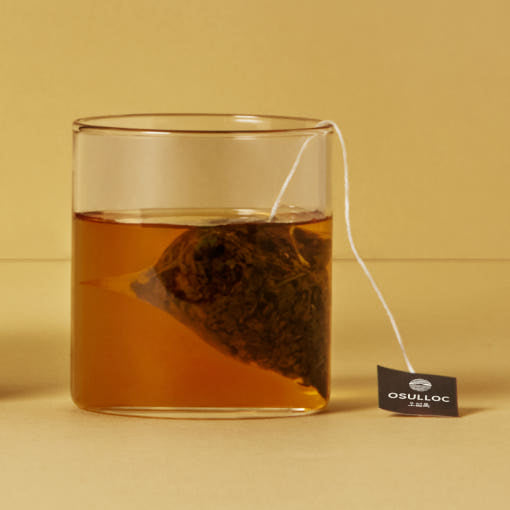 OSULLOC Green Oolong — Pyramid tea bag steeping in a glass of amber tea.