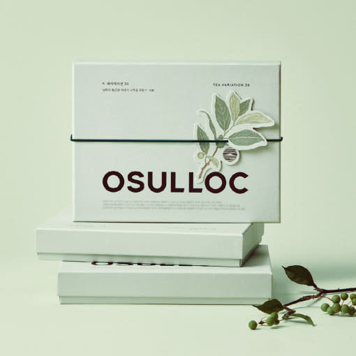 OSULLOC Tea Variation 30 Gift Set — Closed pale green gift boxes stacked beside leafy branches.