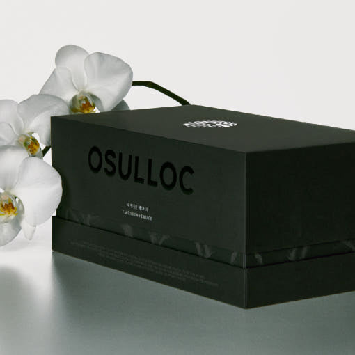 OSULLOC Tea Edition Heritage Gift Set — Closed dark green Heritage chest beside white orchids.