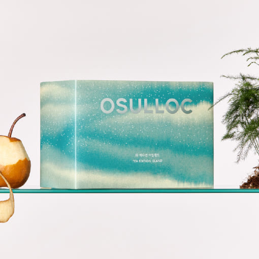 OSULLOC Tea Edition Island Gift Set — Closed turquoise gift box on a glass shelf beside a partly peeled pear and a green plant.