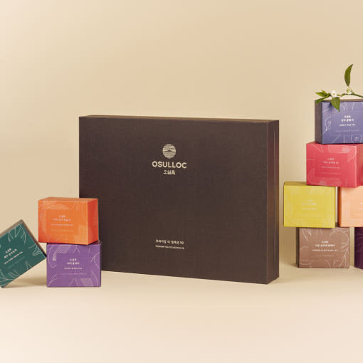 OSULLOC Premium Tea Collection 90 — Closed dark gift box surrounded by small colourful tea boxes.