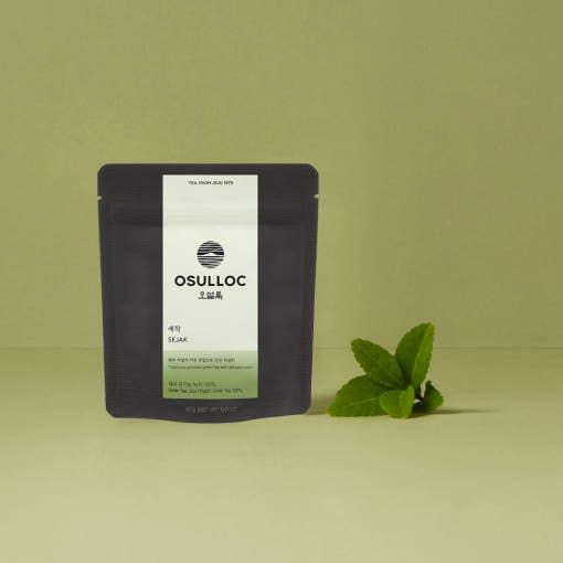 OSULLOC Sejak Green Tea 40 g — Dark pouch beside fresh green leaves on an olive background.